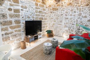 Salón de Casa Señorial Rivadavia con televisión, pared de piedra original y zona de descanso en el centro histórico de Cádiz