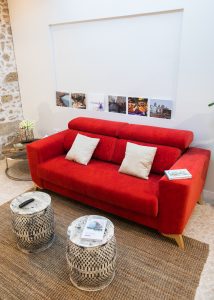 Salón de Casa Señorial Rivadavia con sofá rojo, pared de piedra original y zona de descanso en el centro histórico de Cádiz