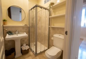 Baño completo con ducha de cristal, lavabo, inodoro y estanterías de almacenaje en Casa Apolo.