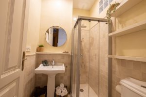 Cuarto de baño con ducha, lavabo, espejo redondo y acabados modernos en el apartamento Casa Apolo.