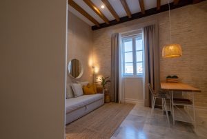 Salón con sofá, comedor y ventana con vistas al centro histórico de Cádiz en Casa Apolo.