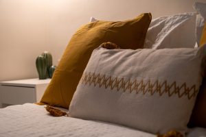 Detalle de la cama con cojines en tonos mostaza y decoración acogedora en el dormitorio de Casa Apolo.