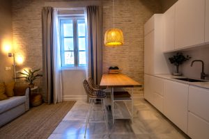 Espacio de salón con sofá, mesa de comedor y ventana con vistas al casco histórico de Cádiz.