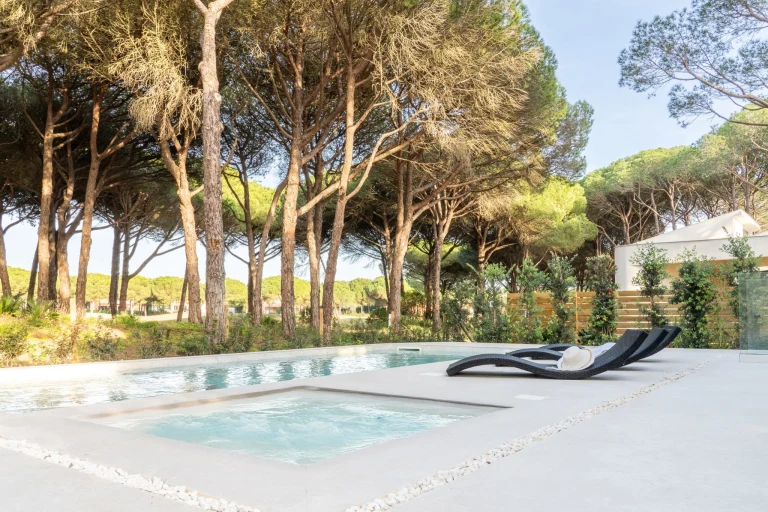 Piscina privada con zona de relax rodeada de pinos en una villa de lujo gestionada por InnCádiz.