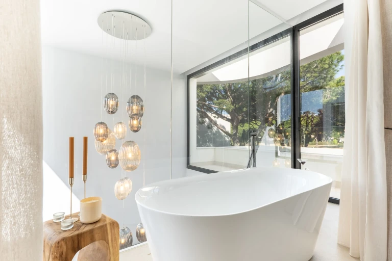 Baño de diseño con bañera exenta y ventanales con vistas al entorno natural de la villa.